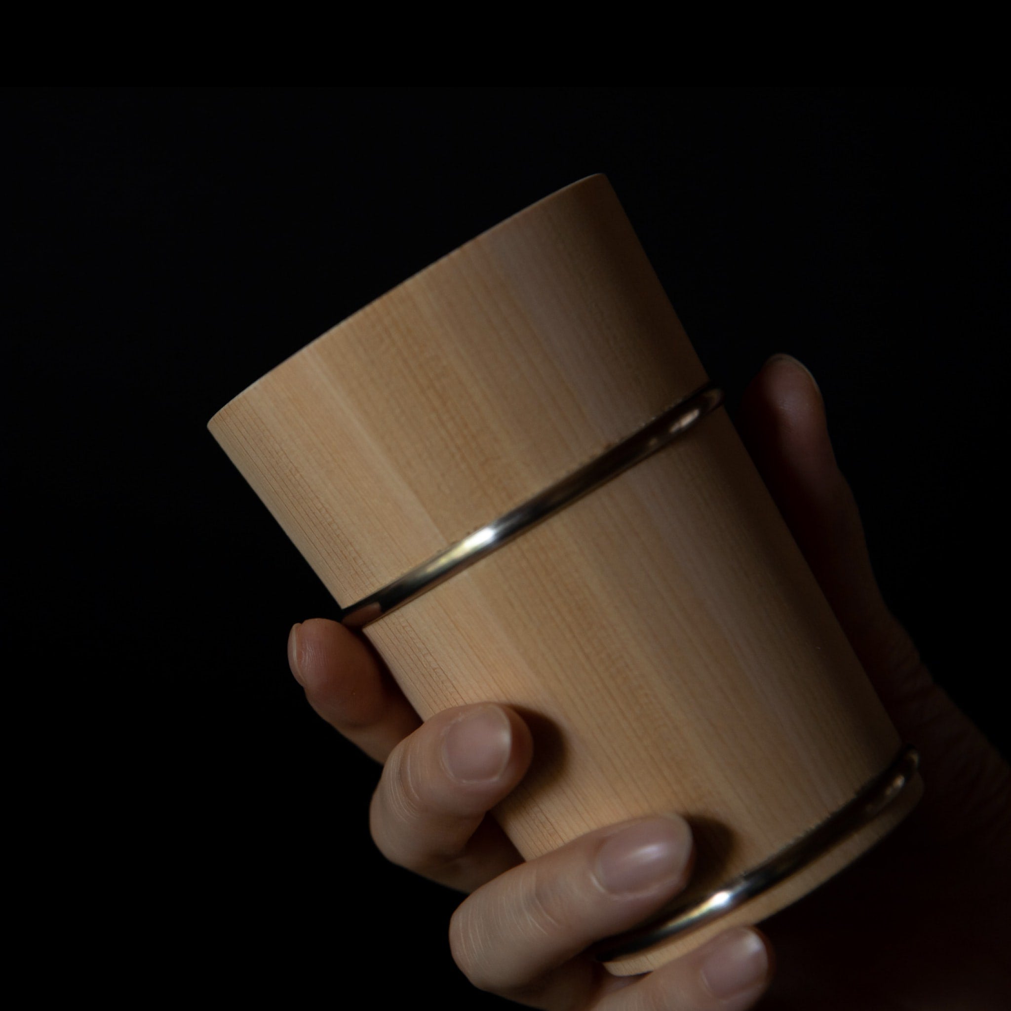 Hand holding wooden Hinoki cup with metal bands