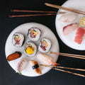 Four pairs of chopsticks resting on plates of sushi