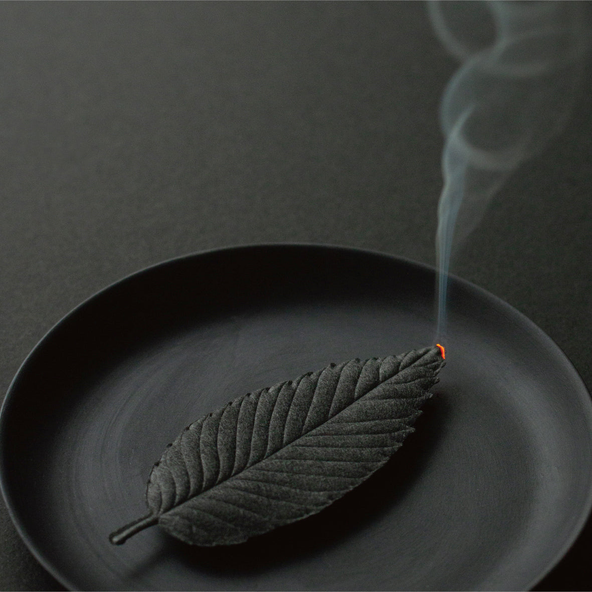 Black incense shaped like a leaf burning on a black plate
