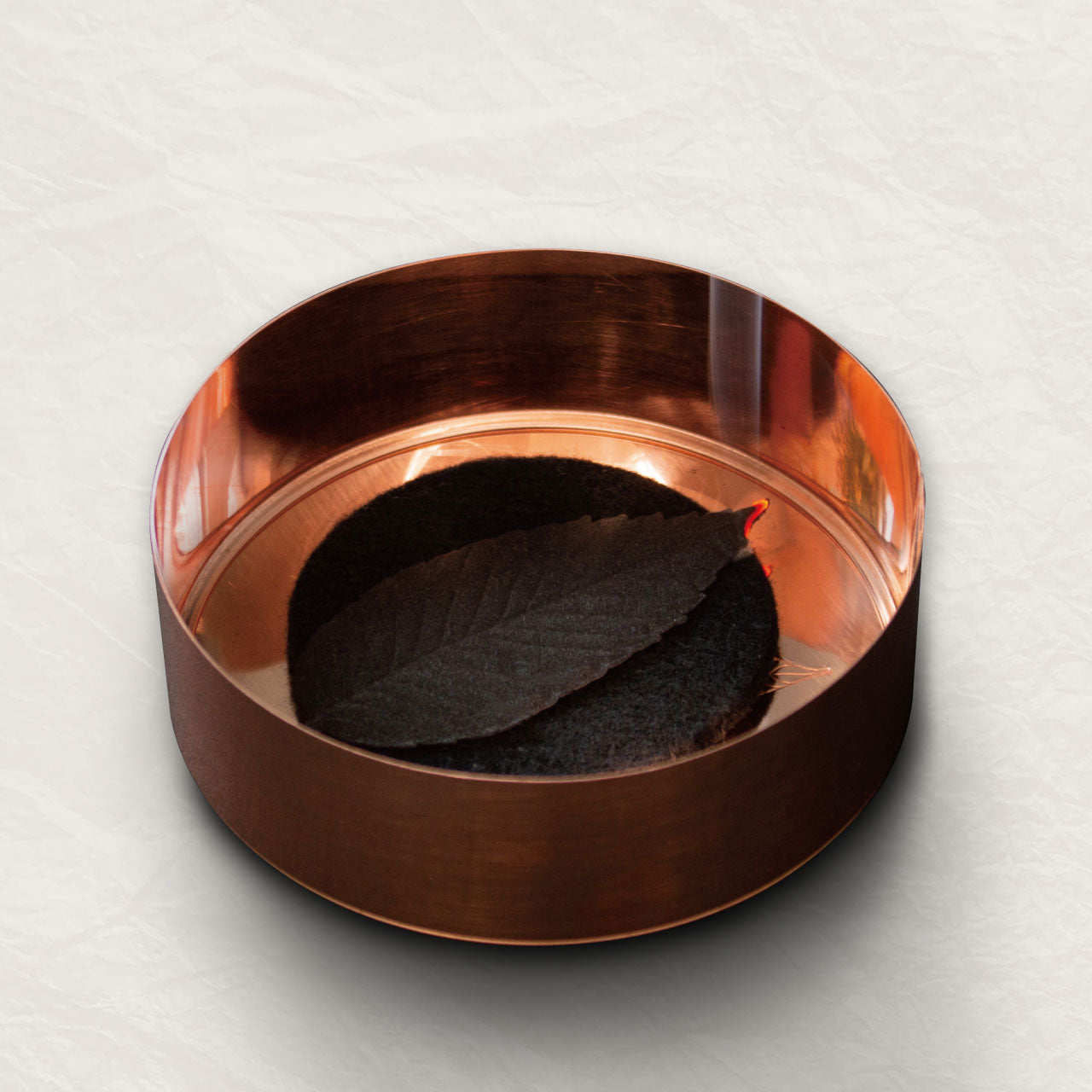 A copper container with black leaf-shaped incense