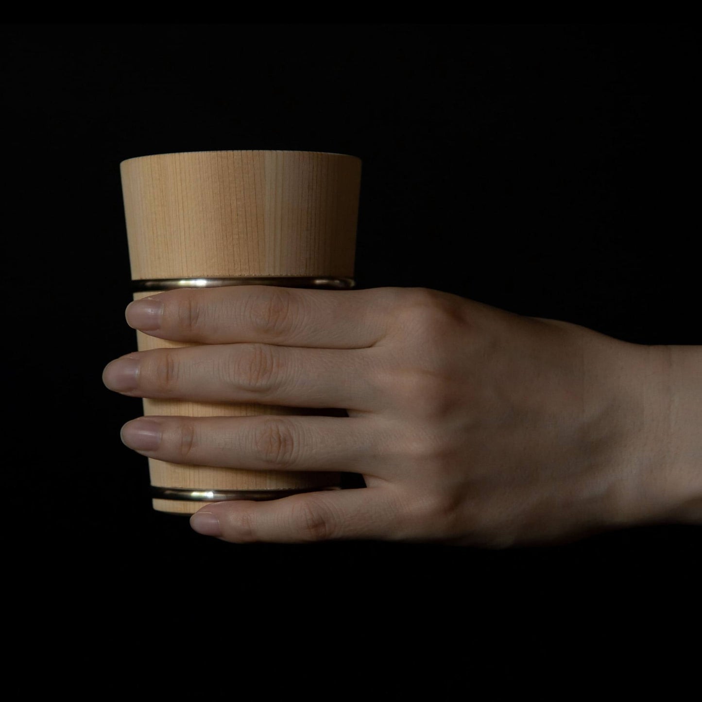 Hand holding wooden Hinoki cup with metal bands