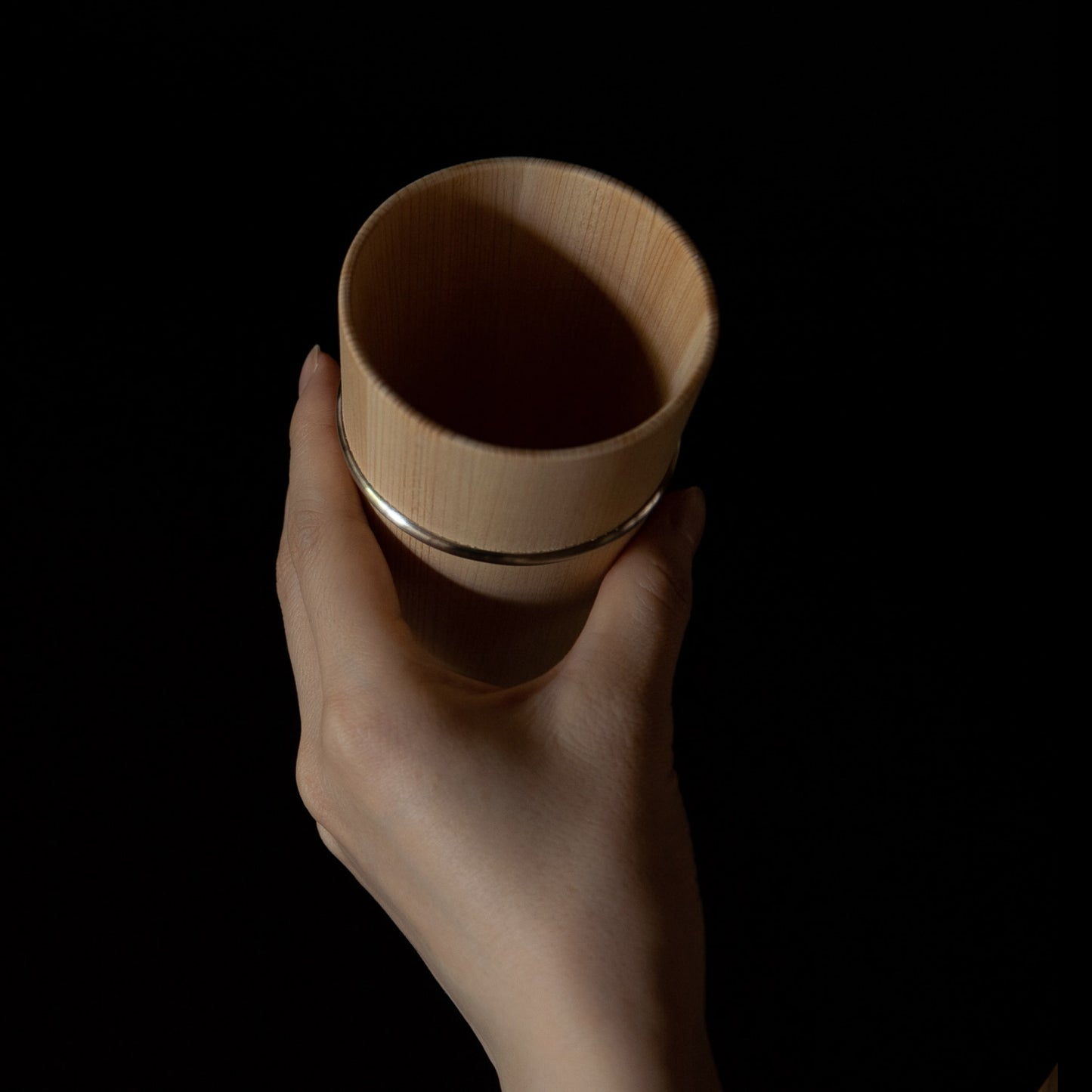 Hand holding wooden Hinoki cup with metal bands