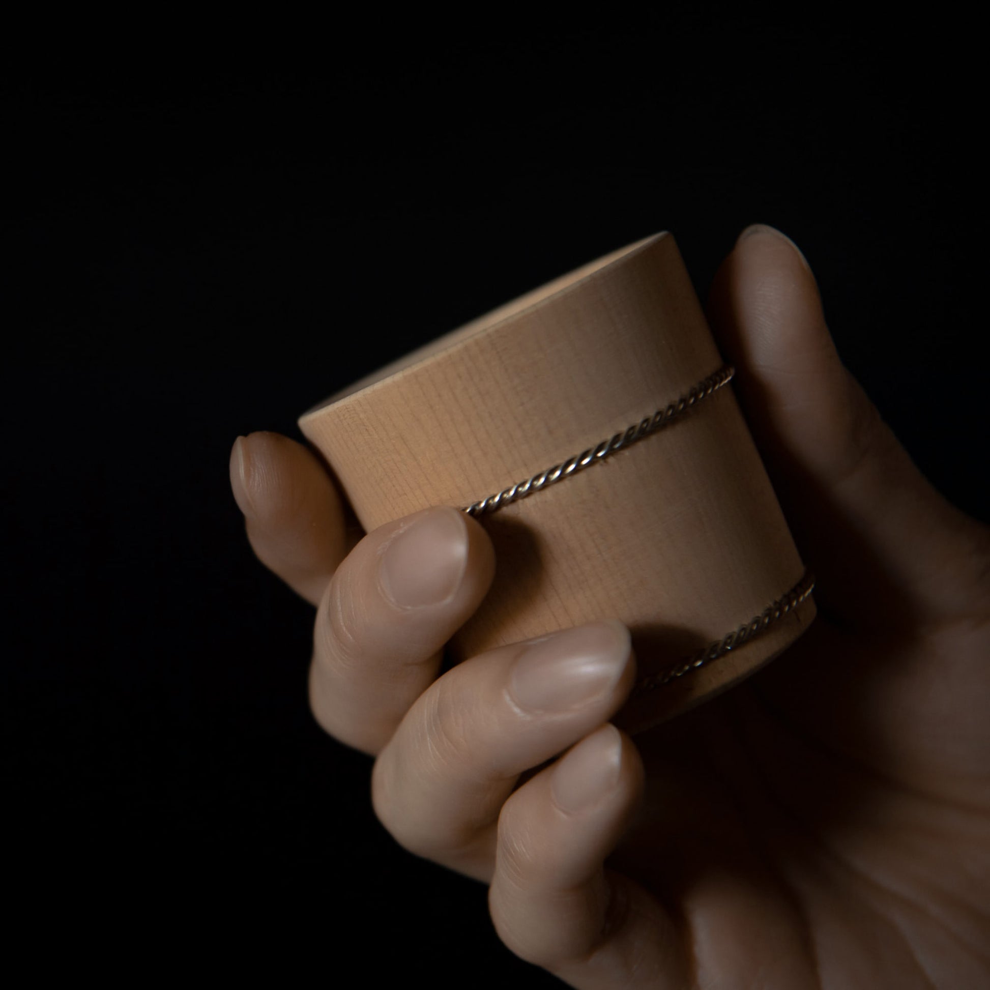 Hand holding wooden Hinoki sake cup with metal bands